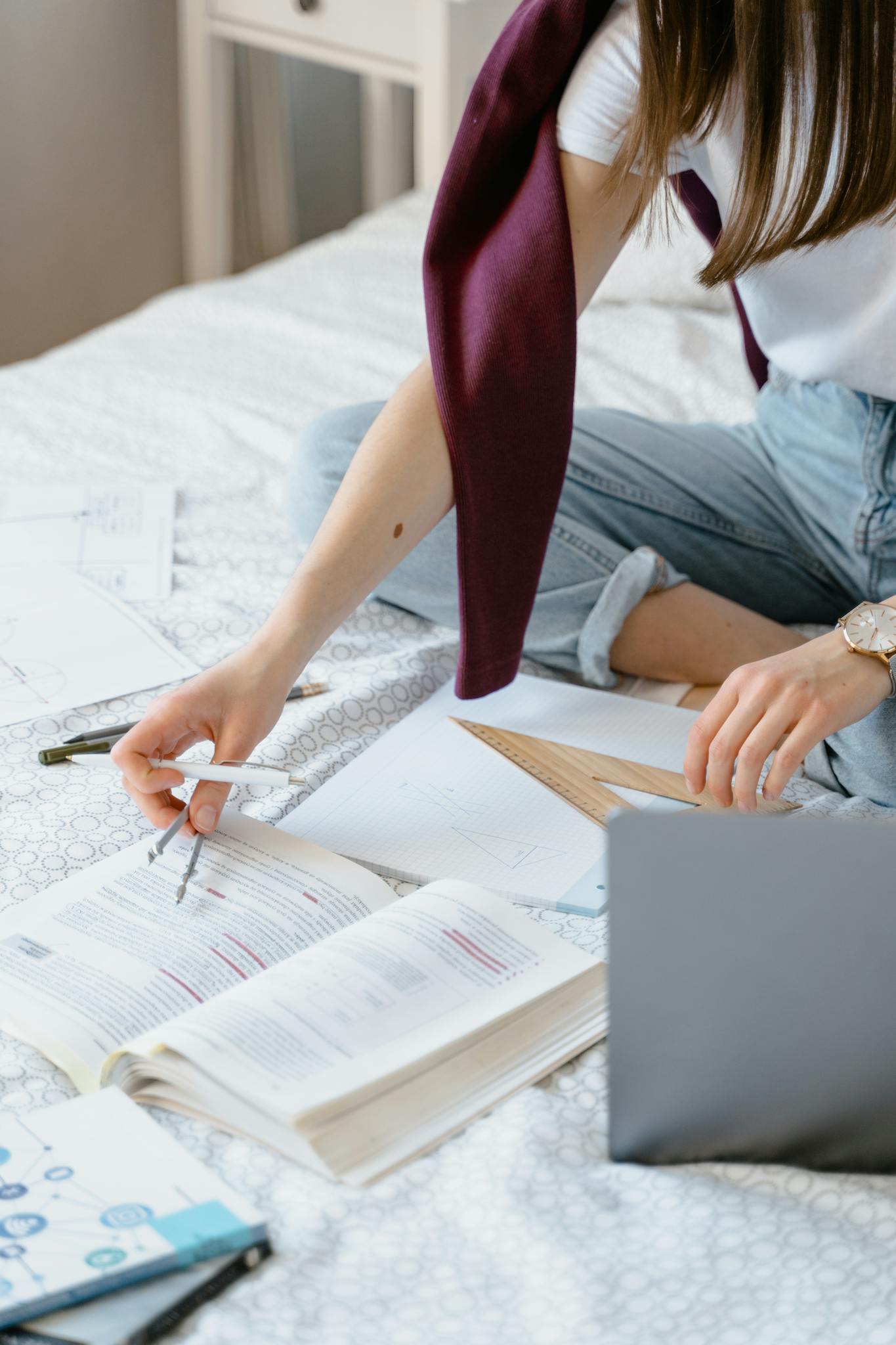 A young woman studies on her bed using a laptop and books, embodying remote learning.